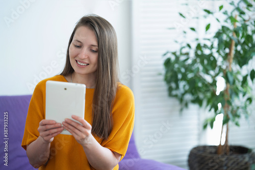 woman sitting on sofa with tablet computer in hands using digital tablet at home