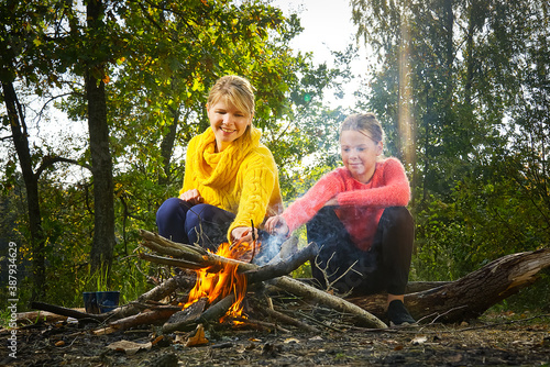 mother and daughter in the autumn forest sitting by the fire. mom and daughter making fire in woods.