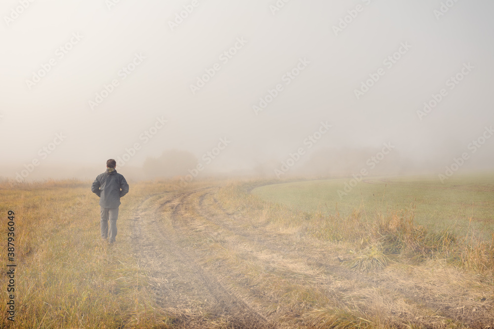 A person walk into the misty foggy countryside, rural road in a dramatic mystic sunrise scene with abstract colors