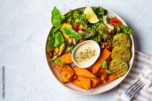 Falafel salad bowl. Vegan lunch plate - baked chickpea patties with baked sweet potatoes and vegetable salad in a white plate, top view.