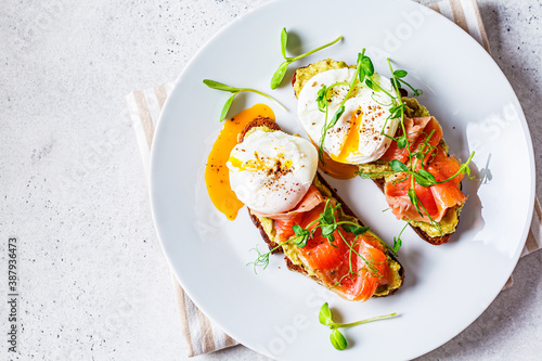 Foto Toast with salmon, poached egg and avocado on white plate, top view
