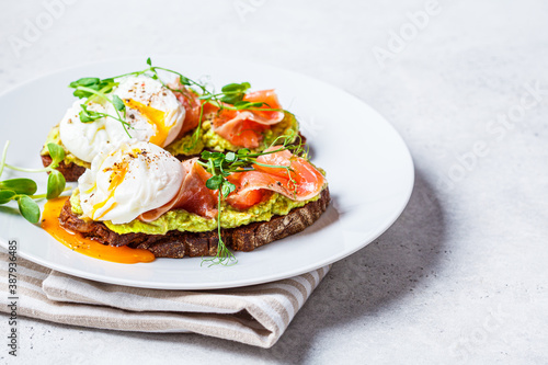 Toast with salmon, poached egg and avocado on white plate. Poached egg with salmon and guacamole on rye bread.