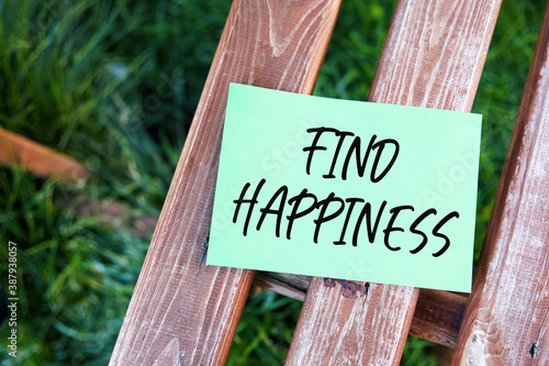 Find happiness inspirational life quote text written on paper on a wooden bench in a garden. © Cagkan