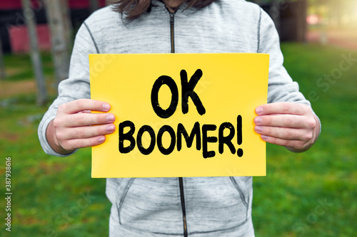 Фотография Teenager holds a banner with the word ok boomer against nature background