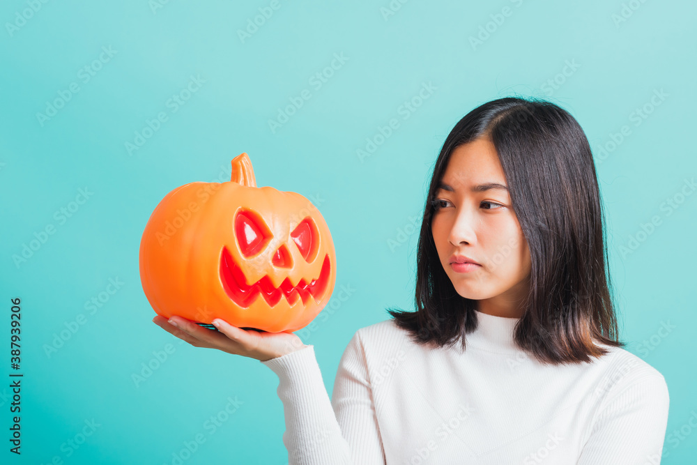 Portrait of Asian beautiful young woman holding orange model pumpkins, funny happy female with ghost pumpkins, studio shot isolated on blue background Portrait of Asian beautiful young woman holding orange model pumpkins, funny happy female with ghost pumpkins, studio shot isolated on blue background