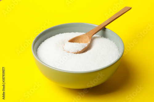 Bowl with salt and spoon on yellow background