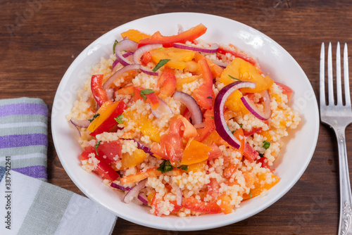 Traditional Mediterranean salad of couscous, tomato, pepper and onion in a plate on a wooden table, close-up - Moroccan and Algerian cuisine