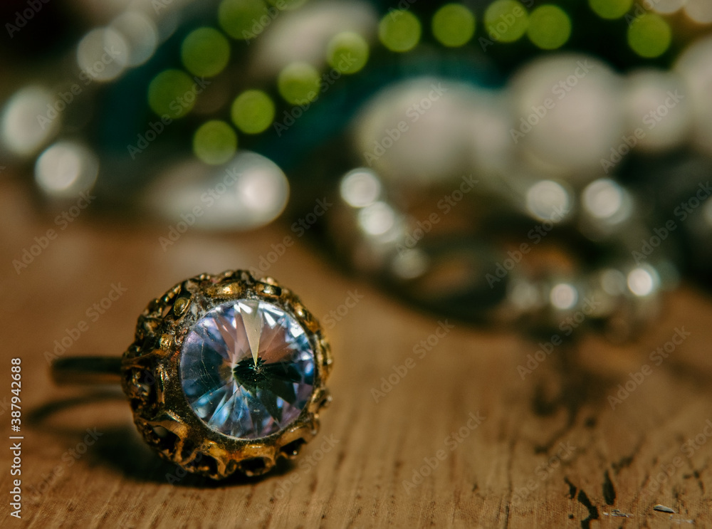 Fototapeta premium Glittering blue-turquoise colored, big ring on brown wooden table top with colorful bokeh background