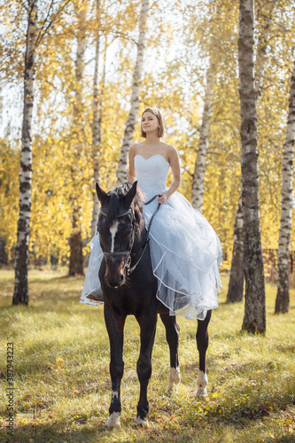 woman in white wedding dress on horseback in autumn park