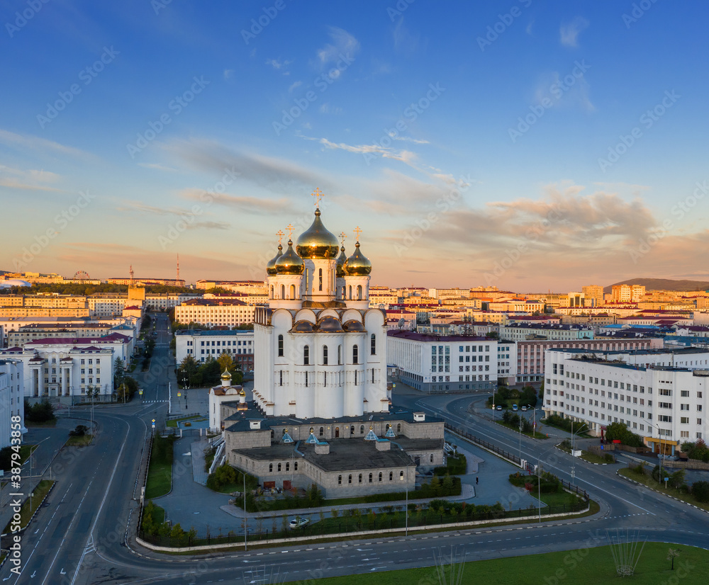 Obraz premium The domes of the cathedral and buildings in the distance are illuminated at sunrise by the first rays of the sun. Beautiful morning cityscape. Trinity Cathedral, Magadan city, Magadan Region, Russia.