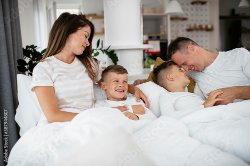 Young family enjoying in bed. Happy parents with sons relaxing in bed