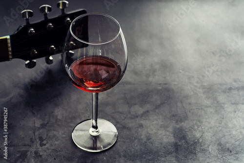 Guitar and high glass with red wine on a stone background.