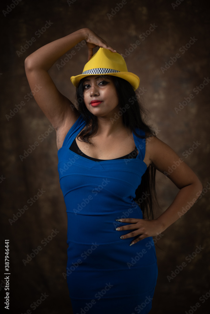 Naklejka premium Studio portrait of an young Indian girl in blue western dress and yellow hat in front of textured background. Fashion portrait photography