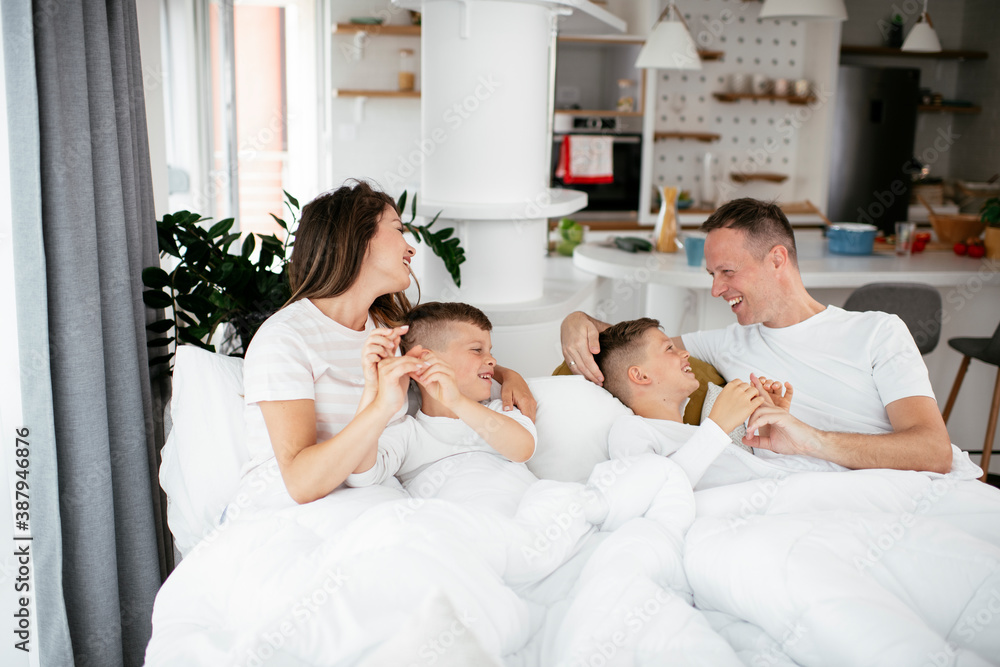 Young family enjoying in bed. Happy parents with sons relaxing in bed Young family enjoying in bed. Happy parents with sons relaxing in bed