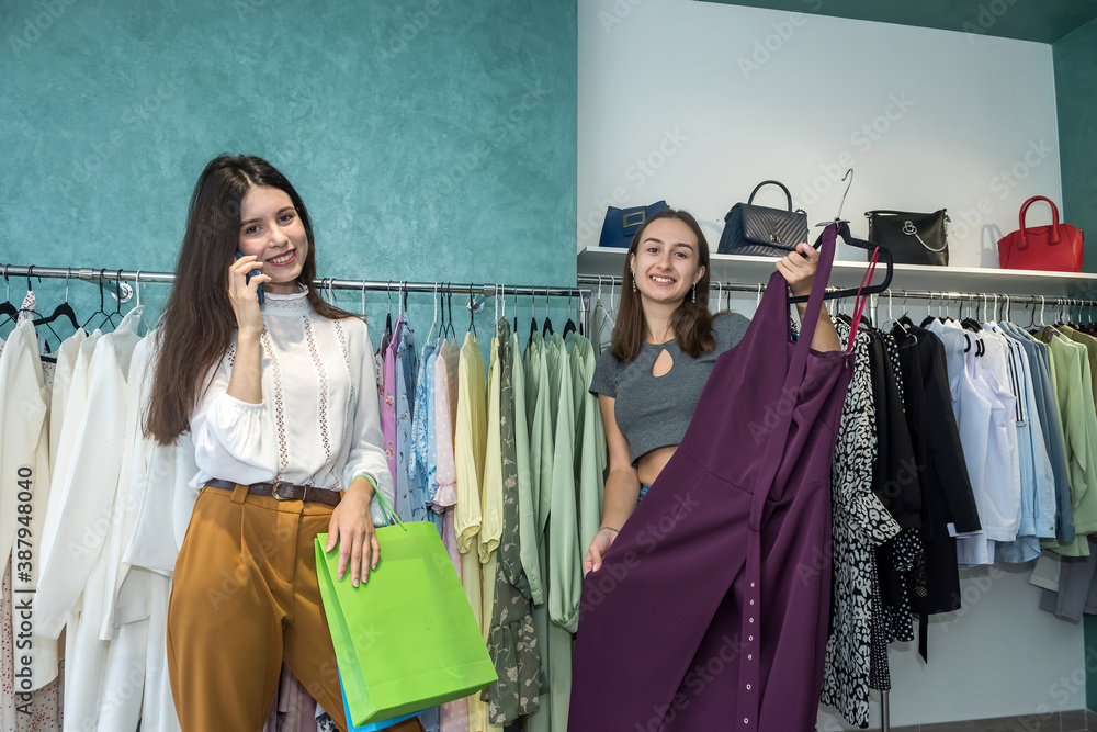 Two women in fashion boutique choose dress. Season holiday discounts for shopping Two women in fashion boutique choose dress. Season holiday discounts for shopping