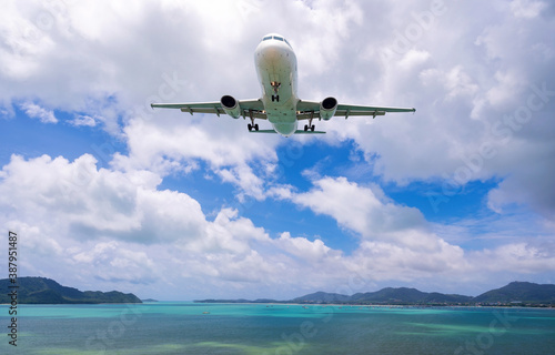 Commercial airplane landing above sea and clear blue sky over beautiful scenery nature background.
