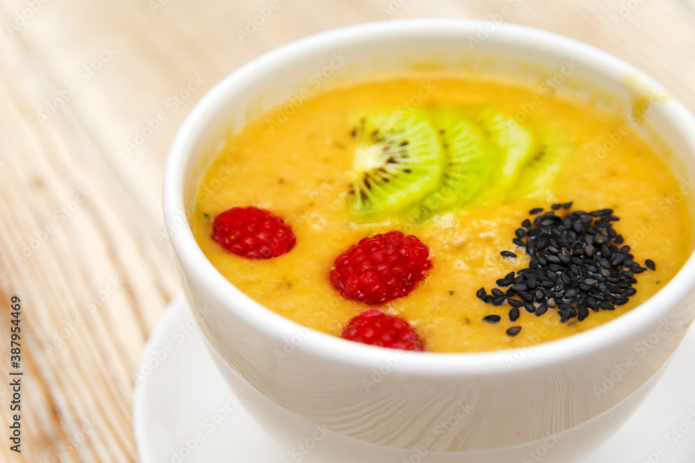 Closeup photot of mango smoothie with kiwi slices, raspberries and chia seeds in a white bowl on a wooden background. Healthy organic food. Selective focus Closeup photot of mango smoothie with kiwi slices, raspberries and chia seeds in a white bowl on a wooden background. Healthy organic food. Selective focus