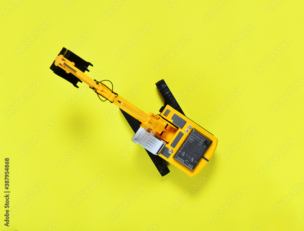 toy yellow excavator with a black bucket on a yellow background. the concept of construction and rental of construction equipment. toy yellow excavator with a black bucket on a yellow background. the concept of construction and rental of construction equipment.
