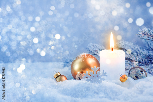 Burning candle and snowy holiday decoration over frosty lights background
