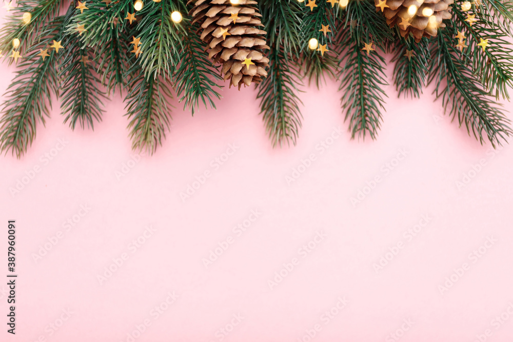 Christmas border with fir branches, conifer cones and gold lights on pastel pink background Christmas border with fir branches, conifer cones and gold lights on pastel pink background