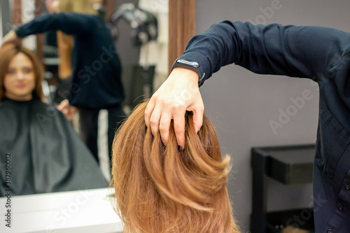 Back view of hairdresser checks red or brown hairstyle of young woman in hair salon