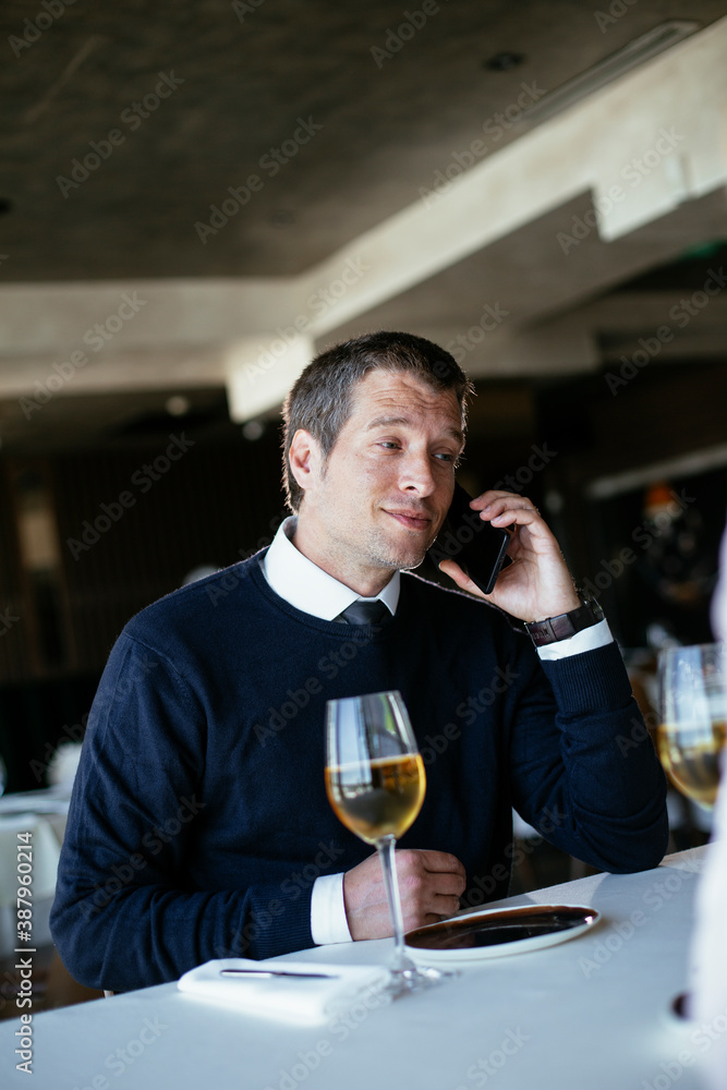 Handsome businessman dressed in the suit drinking wine. Businessman talking to the phone.