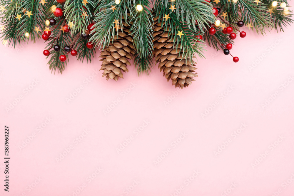 Christmas border with fir branches, conifer cones, red berries and gold lights on pastel pink background Christmas border with fir branches, conifer cones, red berries and gold lights on pastel pink background
