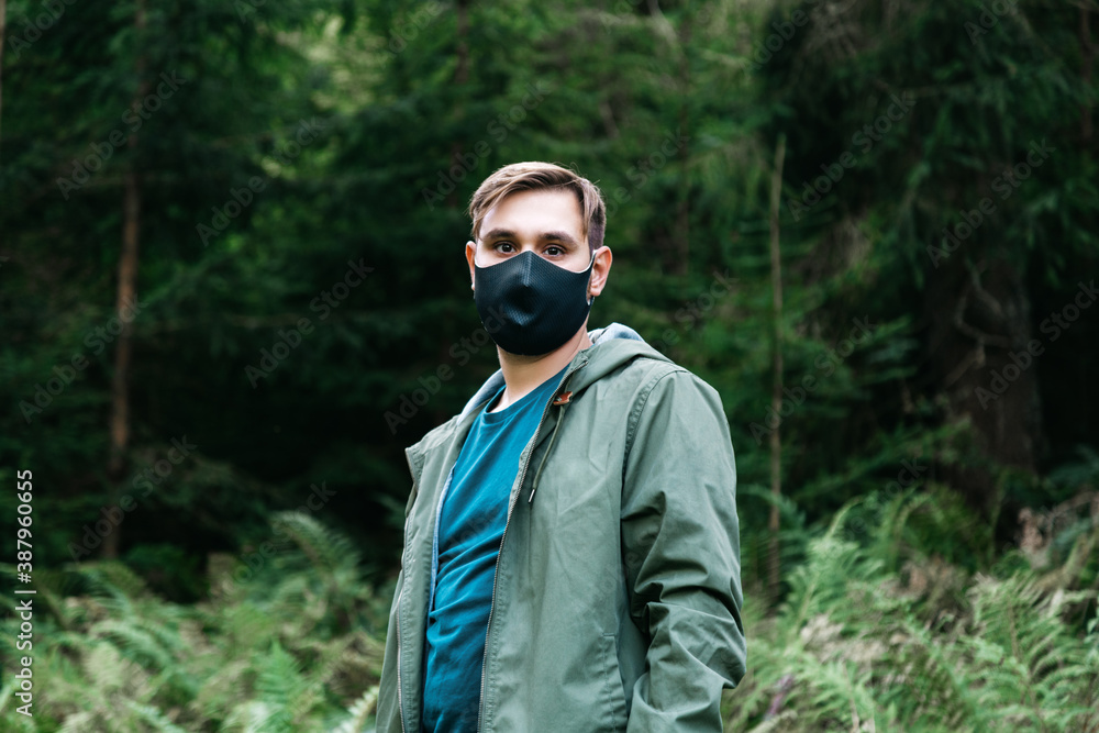 Man in black protective medical mask outside in forest alone. Man travel alone keeping social distance in local tourism. Protection against coronavirus, covid 19 Man in black protective medical mask outside in forest alone. Man travel alone keeping social distance in local tourism. Protection against coronavirus, covid 19