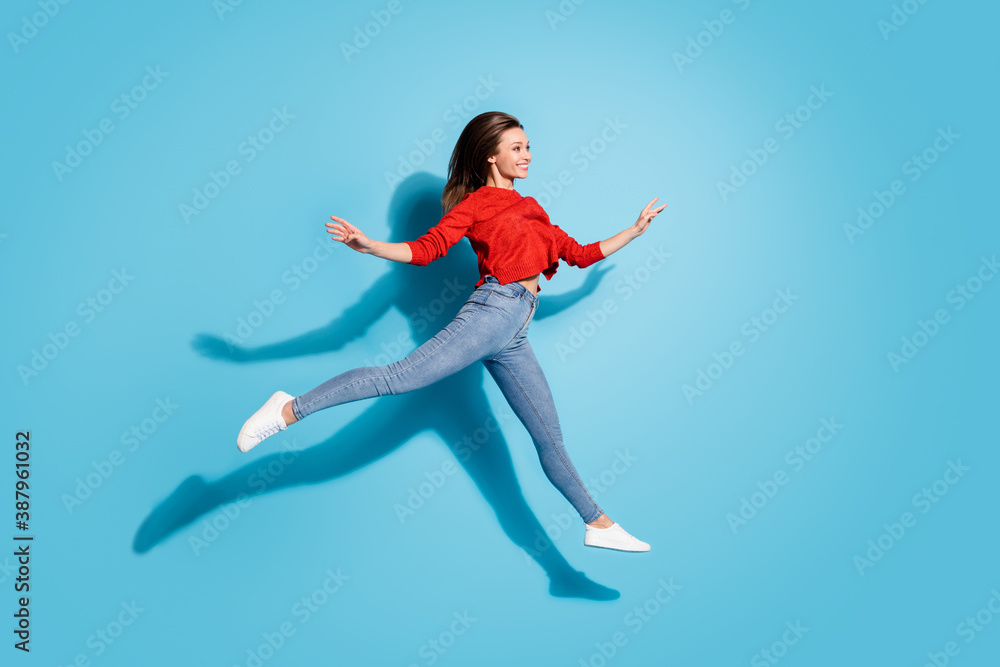 Full length photo of lady jump high moving like ballerina graceful motion shadow isolated blue color background Full length photo of lady jump high moving like ballerina graceful motion shadow isolated blue color background