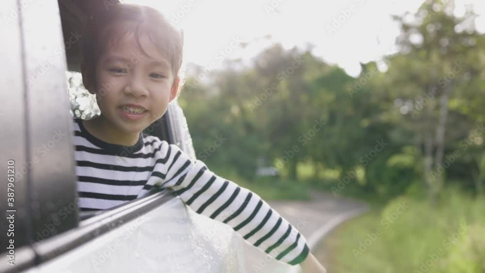 Smiling little Asian girl in car going to summer travel trip.