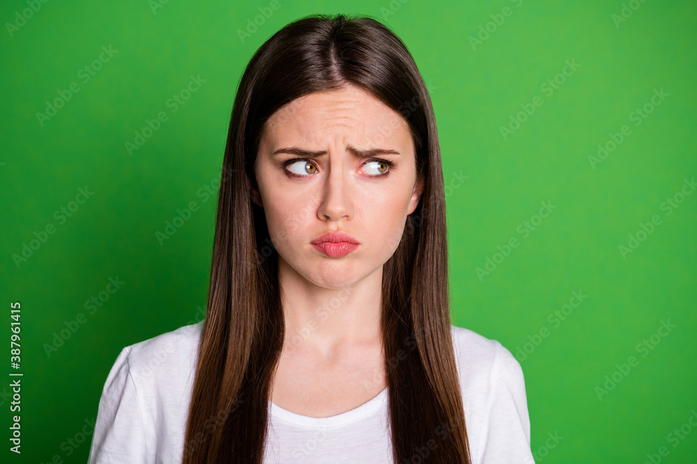 Photo portrait of frowning sad girl looking to side isolated on vivid green colored background Photo portrait of frowning sad girl looking to side isolated on vivid green colored background