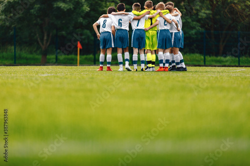 Children in Football Team Huddling. Happy School Boys Standing Together on Grass Soccer Pitch. School Footballers Compete in Youth League Tourament photo