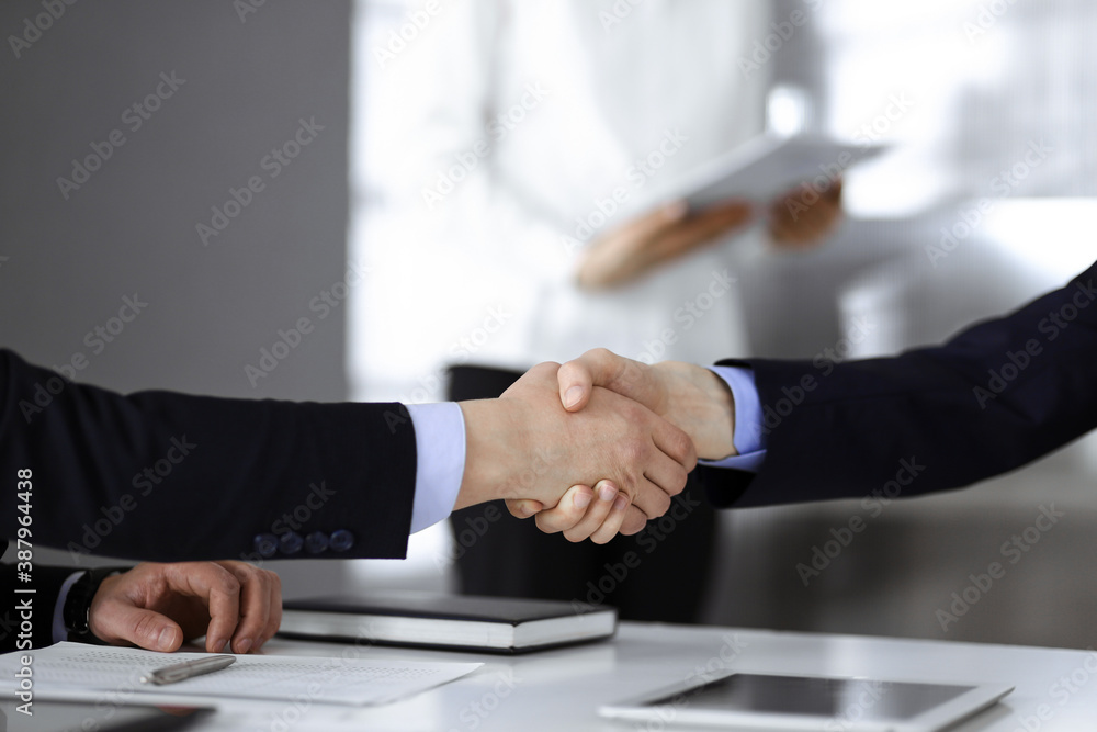 Business people shaking hands at meeting or negotiation, close-up. Group of unknown businessmen sitting at the desk in a modern office. Teamwork, partnership and handshake concept