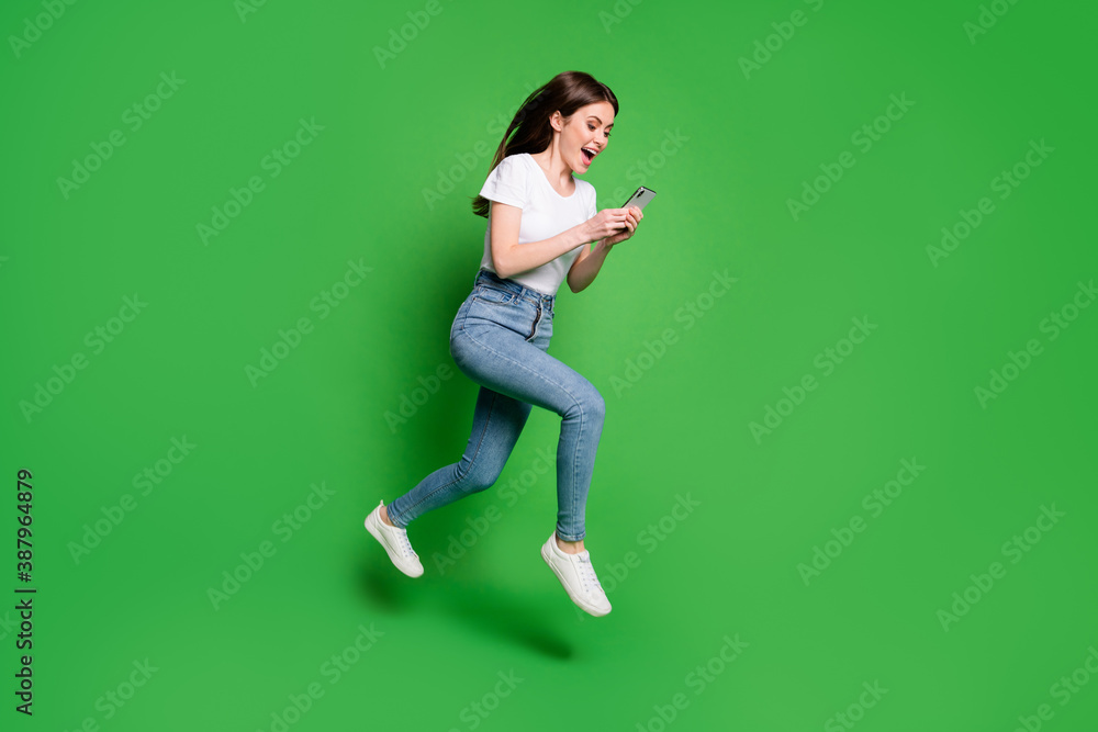 Full body profile side photo of crazy girl jump run read smartphone wear t-shirt denim isolated green color background Full body profile side photo of crazy girl jump run read smartphone wear t-shirt denim isolated green color background
