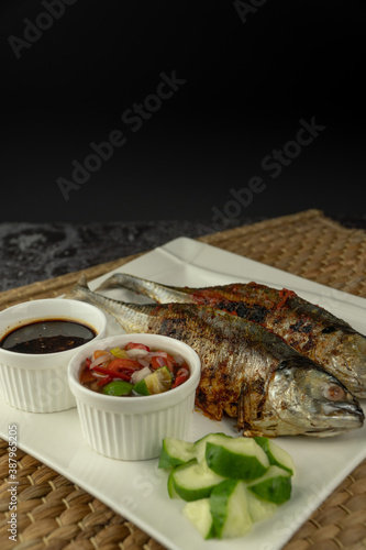 Grilled Torpedo Scad fish (Ikan Cencaru Bakar in Malay) with hot soy sauce, hot tamarind juice and fresh cucumber on white plate photo