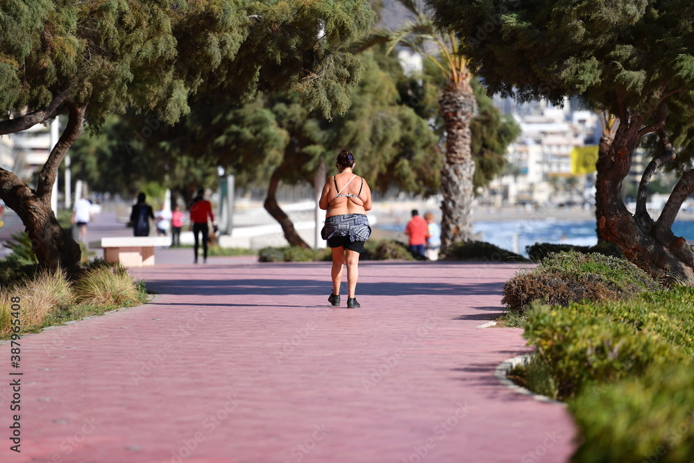 Obraz premium An overweight shirtless woman plays sports on a beach promenade in Benidorm-Spain.