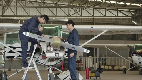 Two young asian aviation maintenance engineer doing a pre flight checkup or maintenance on a small engine aircraft using digital tablet in hangar. Transportation and Technology concept. photo