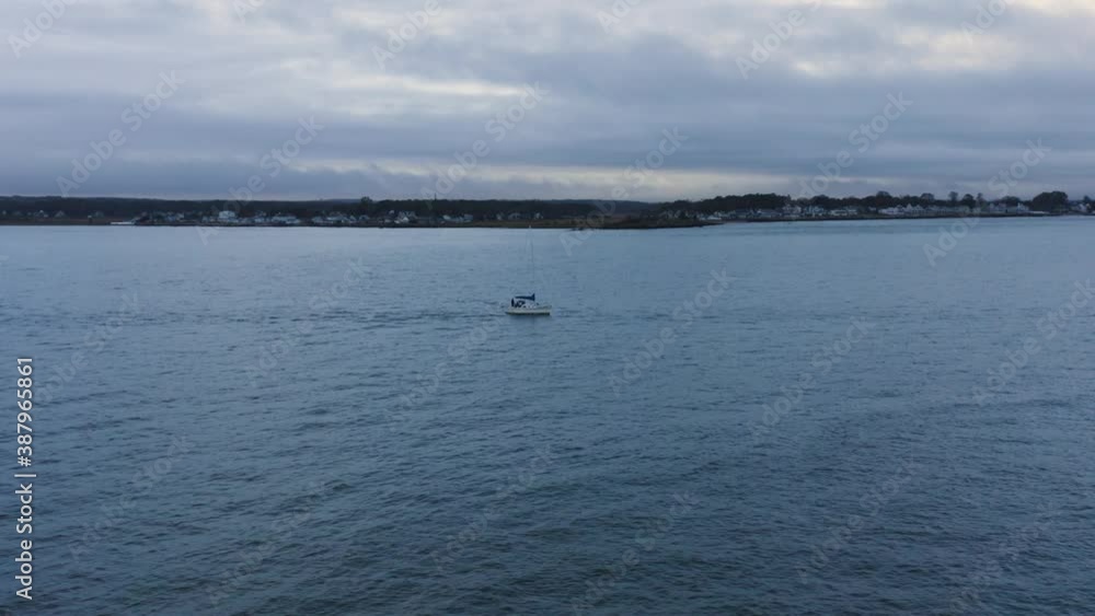 Aerial tracking of sailboat leaving coastal town heading out to cloudy ocean Aerial tracking of sailboat leaving coastal town heading out to cloudy ocean