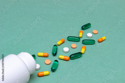 white, green, red and yelloy pills with white bottle on green background. medical concept. concept of genetic illness photo