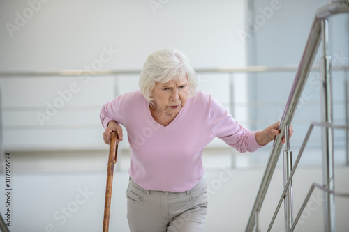 Elderly woman with a walking stick slowly going upstairs photo