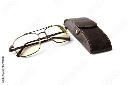 Stylish eyeglasses with yellow toned lenses lie on white background next to the hard case made of genuine brown leather. Isolation