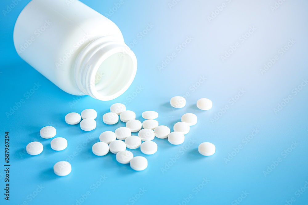 Close up of teblets pills spilling from Plastic pill bottle on blue background with selective focus Close up of teblets pills spilling from Plastic pill bottle on blue background with selective focus