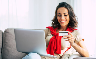 Beautiful happy young woman in casual clothes is sitting on the couch at home and doing online shopping on black friday.