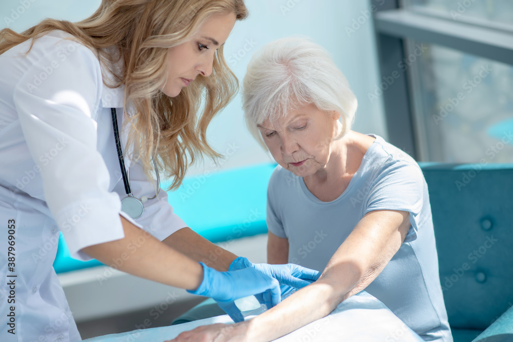 Obraz premium Long-haired smiling nurse making injection to an elderly woman