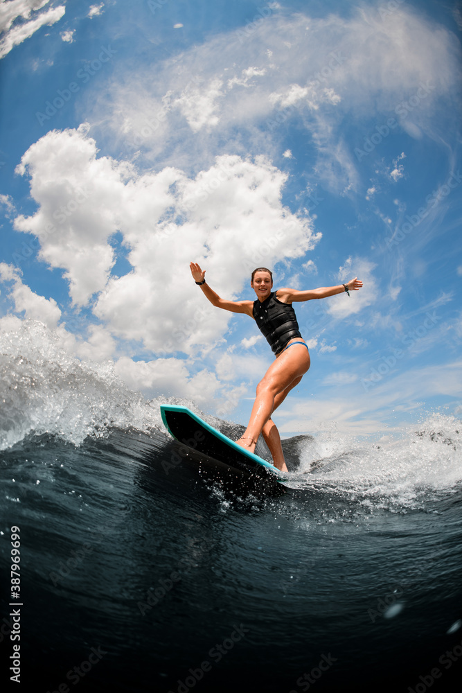 Attractive woman riding on the board wake surfing on the river against the cloudy sky