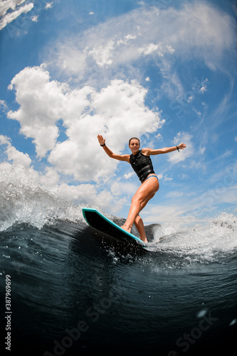 Attractive woman riding on the board wake surfing on the river against the cloudy sky © fesenko