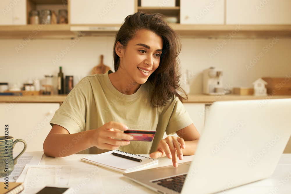 Cute Arabic girl transferring money with online banking using wireless internet connection on laptop. Stylish young woman holding debit card entering personal payment data, purchasing goods distantly Cute Arabic girl transferring money with online banking using wireless internet connection on laptop. Stylish young woman holding debit card entering personal payment data, purchasing goods distantly