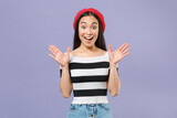Excited surprised young brunette asian woman wearing striped t-shirt red beret standing keeping mouth open spreading hands looking camera isolated on pastel violet colour background studio portrait.