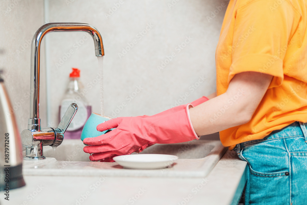 A woman in casual clothes and pink rubber gloves is washing dishes. Side view. Housework