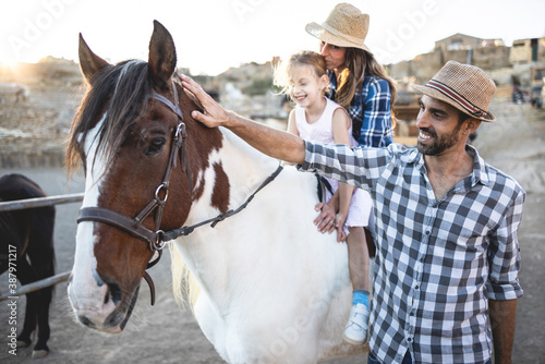 Happy parents with daughter riding a horse at farm ranch - Family lifestyle and animal love concept - Focus on father face